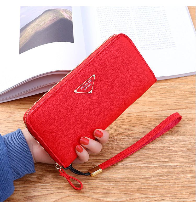 Red casual single pull ladies wallet with lychee pattern and zipper clutch strap on wooden table with book background