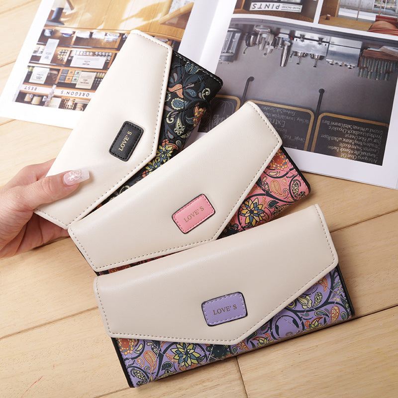Three BIRDS wallets for women in PU leather with floral embroidery patterns and zipper buckle closures on a wooden surface.