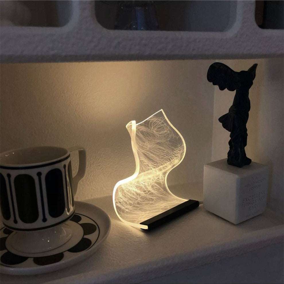 Warm high appearance level bedside lamp glowing softly on shelf next to cup and decorative statue