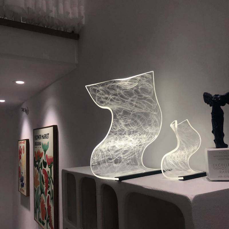 Warm high appearance level bedside lamp with abstract modern design glowing in white light on a table in a minimalist room