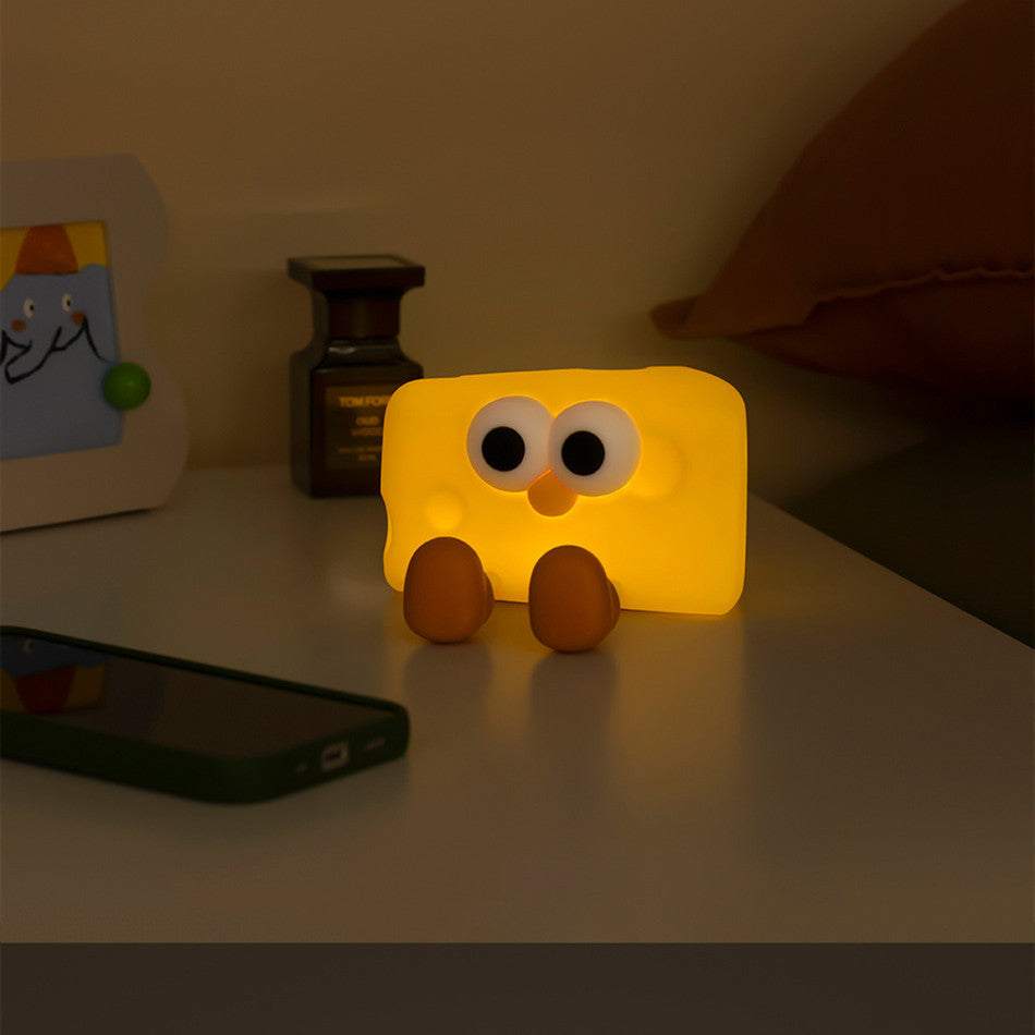 Cute silicone cheese small night lamp glowing on bedside table with eyes and feet design