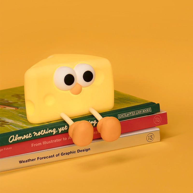 Cute silicone cheese small night lamp with eyes and legs sitting on books against yellow background