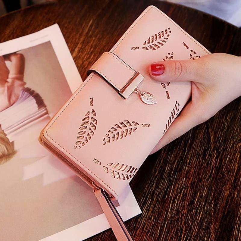 Pink women's wallet purse with leaf cut-out design and clasp closure on wooden table