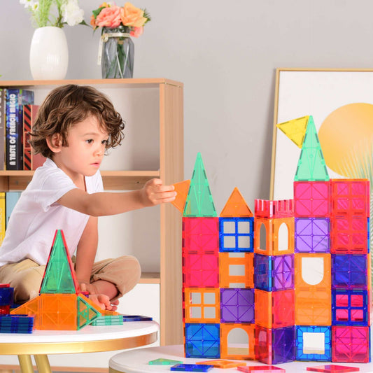Child playing with colorful Magnetic Tiles Building Blocks creating a tower structure on a white table in a cozy room