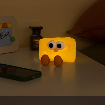 Cute silicone cheese small night lamp glowing on bedside table with eyes and feet design