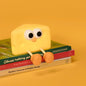 Cute silicone cheese small night lamp with eyes and legs sitting on books against yellow background