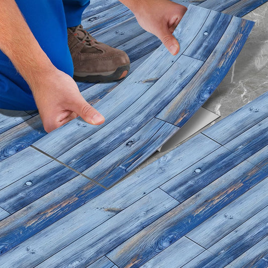 Person installing blue wood grain peel and stick floor tiles on gray surface