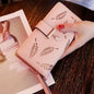 Pink women's wallet purse with leaf cut-out design and clasp closure on wooden table