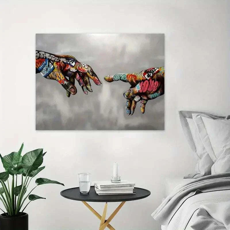 Modern canvas graffiti wall art featuring colorful spray-painted hands reaching toward each other on a gray background, displayed in a minimalist living space with a round table and plant.